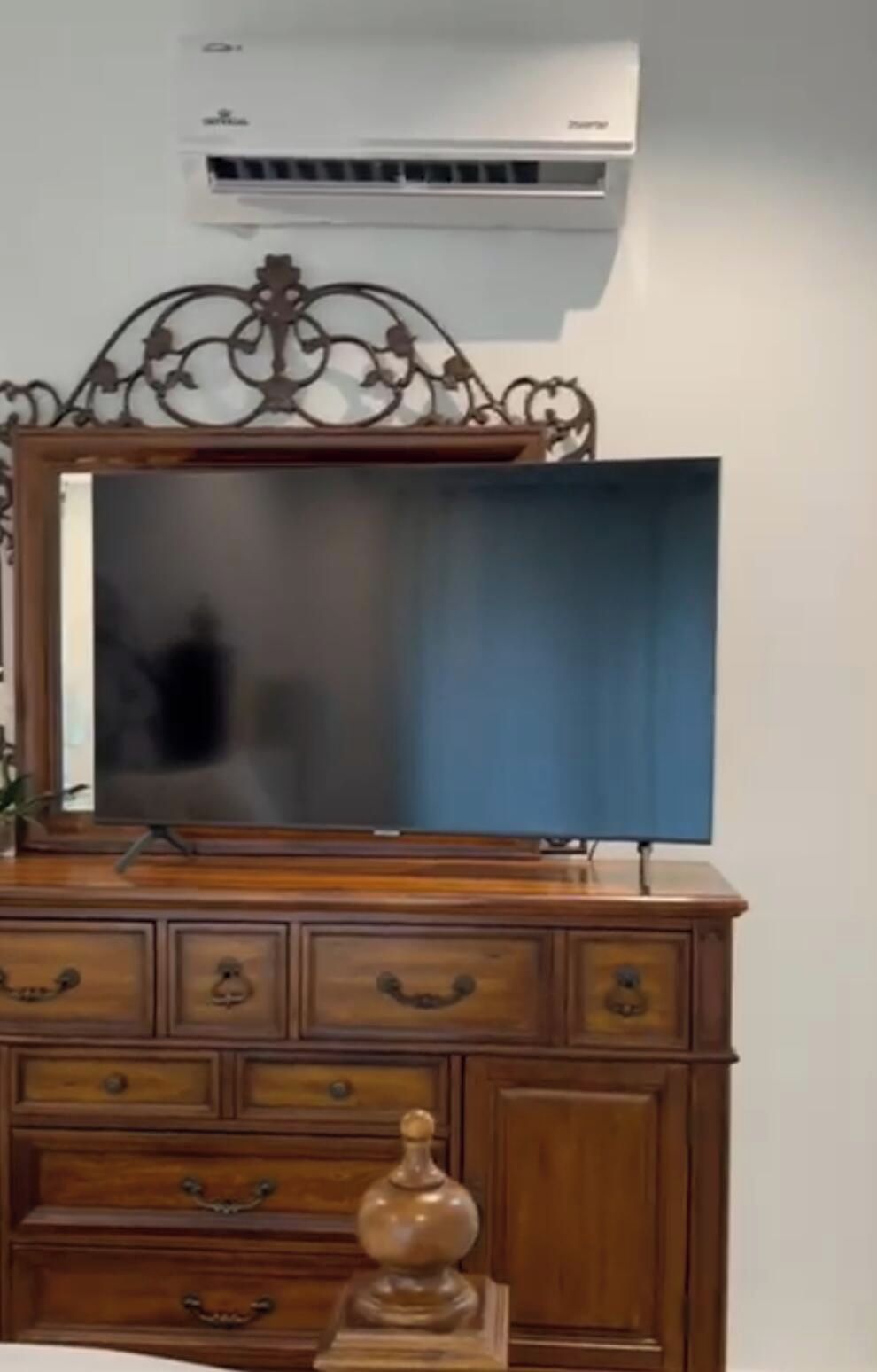 Une commode en bois, un téléviseur à écran plat, un miroir décoratif et un petit vase.