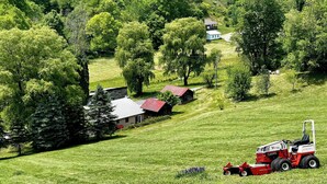 Paesaggio rurale con un trattore rosso, case e vegetazione rigogliosa.