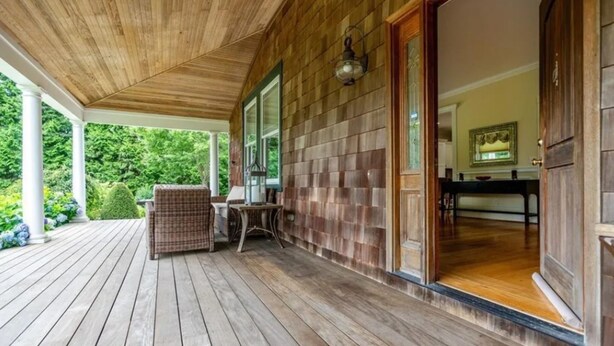Een houten terras met tuinmeubilair, een overdekte veranda en uitzicht op een weelderige tuin.
