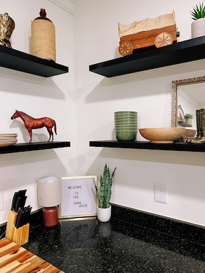A kitchen with black countertops, wooden shelves, a horse figurine, a welcome sign, and a potted plant. - Nice 3-bedroom house with AC in charming Madisonville (Madisonville)