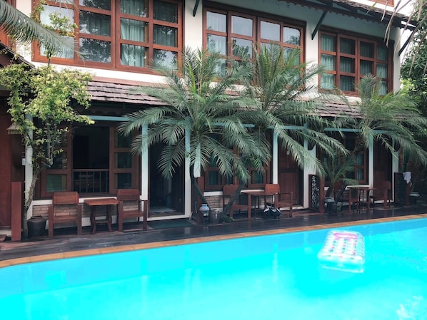 A poolside area with a pool, wooden furniture, and palm trees. - Room-503 Serene Teak Boutique Apartments (Chiang Mai)
