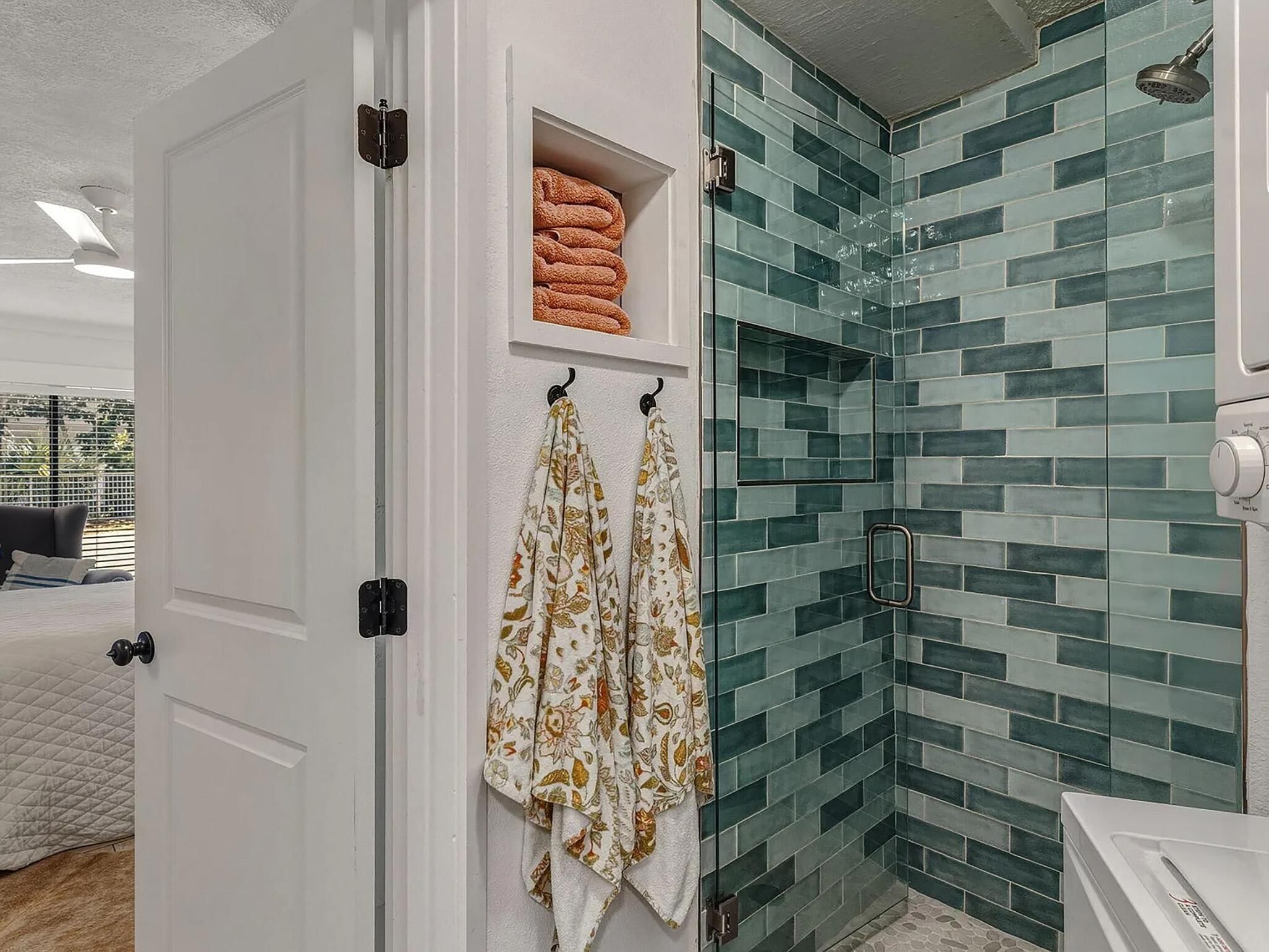 Une salle de bain avec une douche à parois de verre, un porte-serviettes orné de serviettes à motifs et une étagère avec des serviettes pliées.