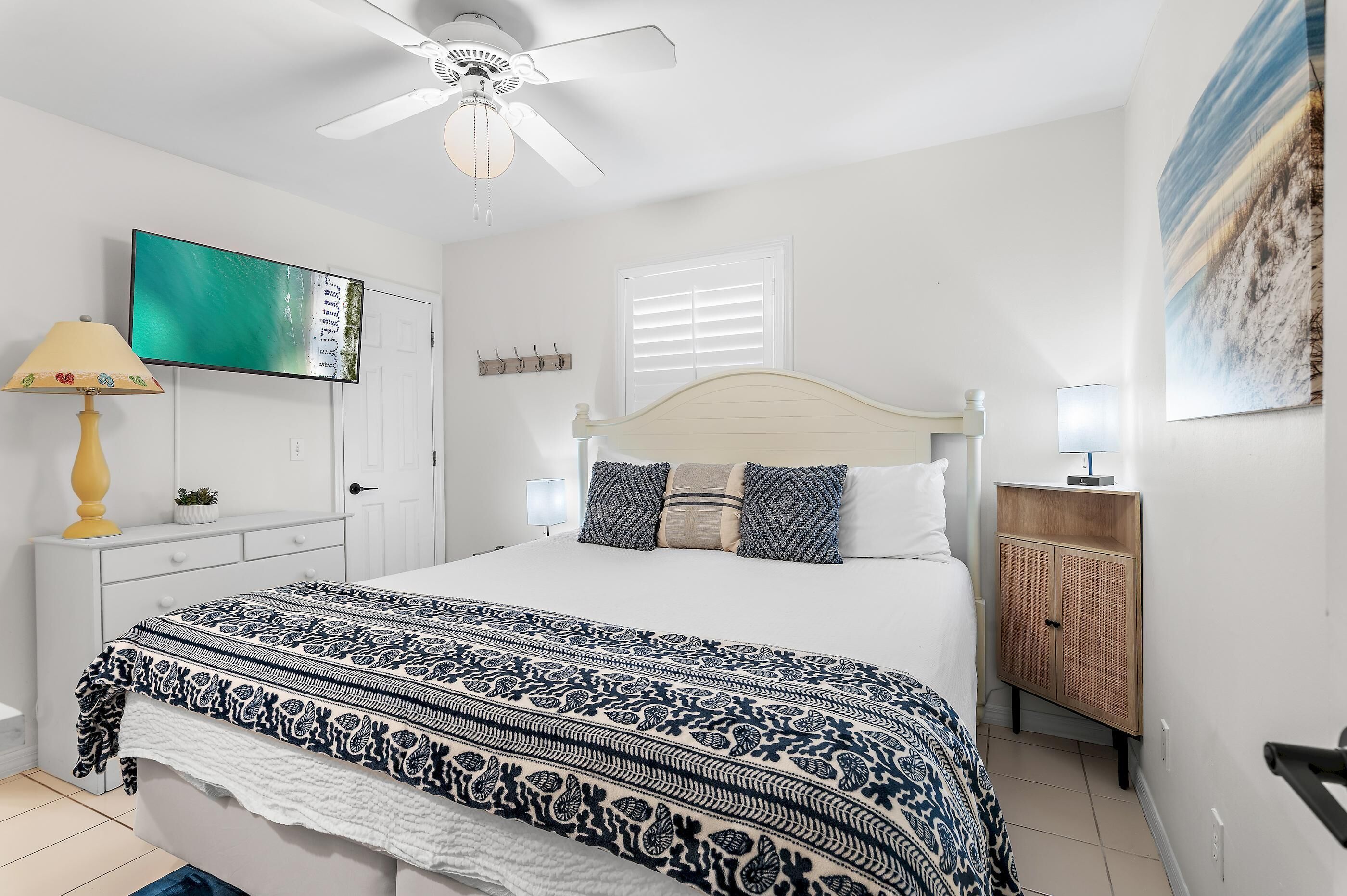 A bedroom with a bed, a ceiling fan, a TV, a cabinet, and a window.