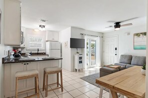 Eine moderne Küche mit weißen Schränken, einer schwarzen Arbeitsplatte und einem Essbereich mit einem Holztisch und zwei Barhocker.