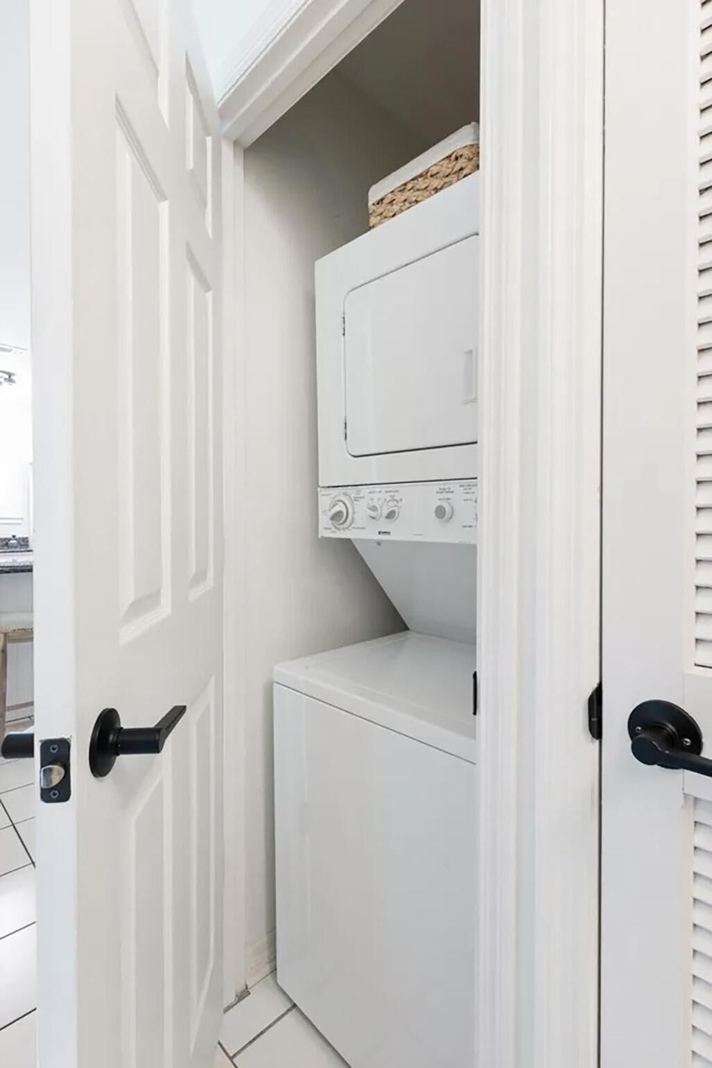 Un lavadero con lavadora y secadora, una puerta blanca y un estante pequeño con una cesta.