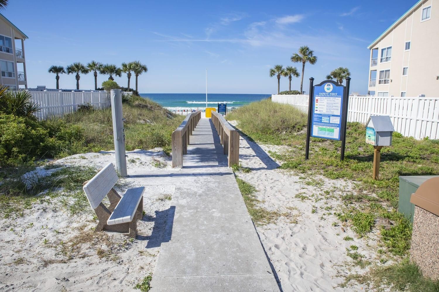 A beach path leading to the ocean with a safety sign, benches, and a fence.