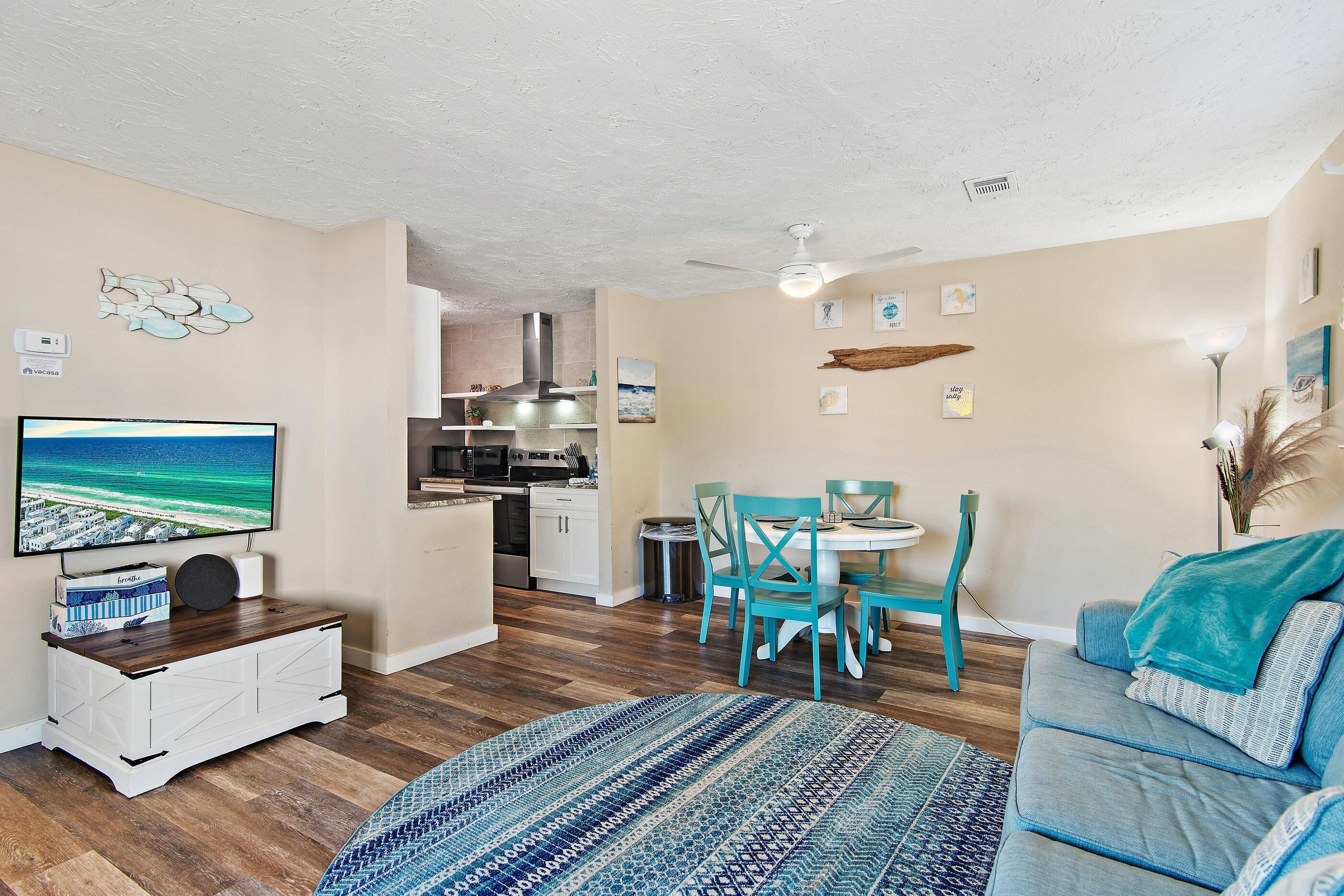 A living room with a TV, a dining area with chairs, a sofa, and a kitchen in the background.