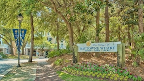 A sign for The Village of Baytowne Wharf with a pathway leading to a building. - Cross Creek 29D (Miramar Beach)