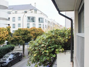 Uma rua residencial com um carro estacionado, um edifício com várias janelas e uma árvore com folhas verdes.