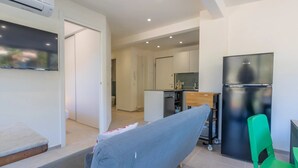 Una sala moderna con un sofá, un televisor de pantalla plana, una cocina con refrigerador y una mesa de comedor.
