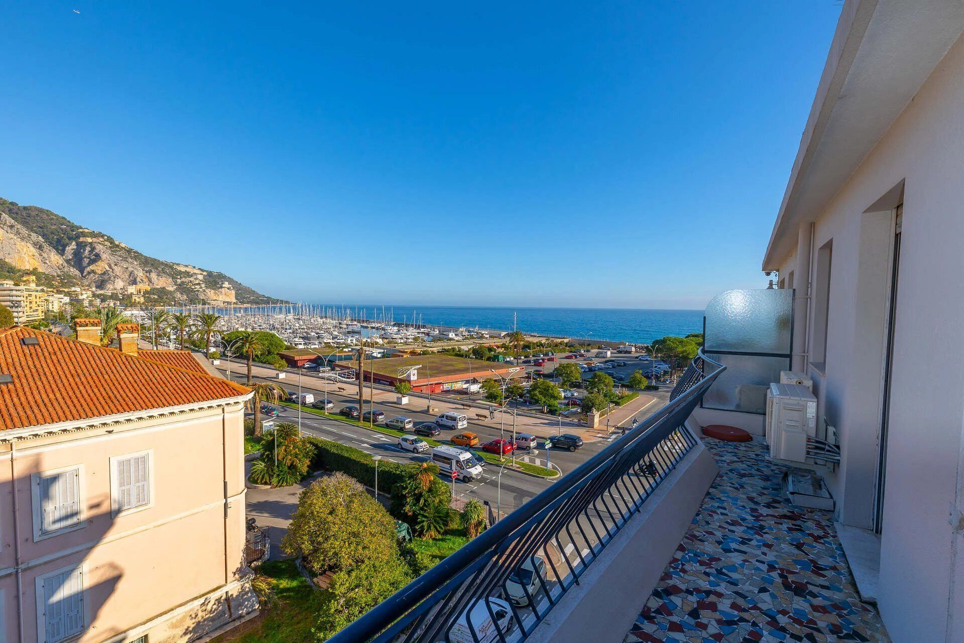 A balcony with a view of a marina, buildings, and a hilly landscape.