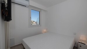 Un dormitorio con una cama, una ventana, un radiador y un televisor montado en la pared.