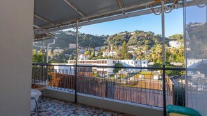 Un balcón con vistas a un pueblo en la ladera, suelo de baldosas y barandilla metálica.