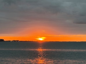 Ein Sonnenuntergang über einem Gewässer mit einer entfernten Küstenlinie.