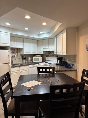 A kitchen with white cabinets, a dining table, and chairs. - Beachfront Cozy 2-bedroom 1- bath condo with AC in serene South Padre Island. (South Padre Island)