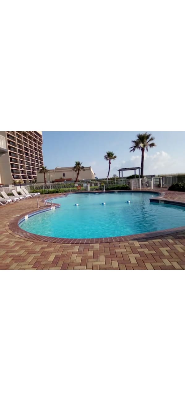 Ein Pool mit Liegestühlen, Palmen und einem Gebäude im Hintergrund.
