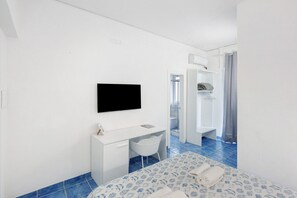 A hotel room with a bed, a desk, a chair, a TV, and a bathroom visible through an open door. - La Vesuviana – Deluxe Room 2 with Balcony, Wi-Fi and Air Conditioning (Castellammare di Stabia)