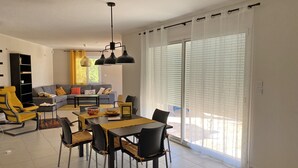Una sala de estar moderna con comedor, un conjunto de sofás y un amplio ventanal corredera al exterior.