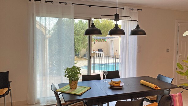 Un comedor con una mesa, sillas, una planta y vistas a una piscina.