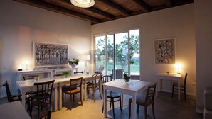 Un comedor con mesas y sillas de madera, un ventanal con vistas a zonas verdes y obras de arte en las paredes.