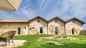 Una hilera de edificios de piedra con múltiples ventanas y puertas, un césped y una silla de mimbre.