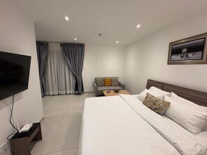 A hotel room with a bed, a sofa, a TV mounted on the wall, and a painting. - Executive Studio at Bantree, 10minutes from Airport (Accra)