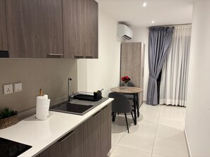 Eine moderne Küche mit Einbauherd, ein kleiner Essbereich mit Tisch und Stühlen sowie ein Blick ins Freie durch ein Fenster mit Vorhängen.