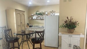 Cocina compacta con una mesa de comedor, sillas, un refrigerador y un pequeño mueble con una planta.
