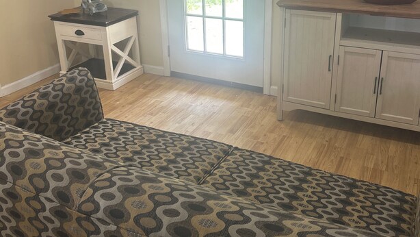 Un salón con un sofá estampado, una mesita auxiliar, un armario y una puerta que da al exterior.