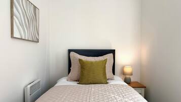 A neatly made bed with a quilted cover, a bedside lamp, and a radiator.