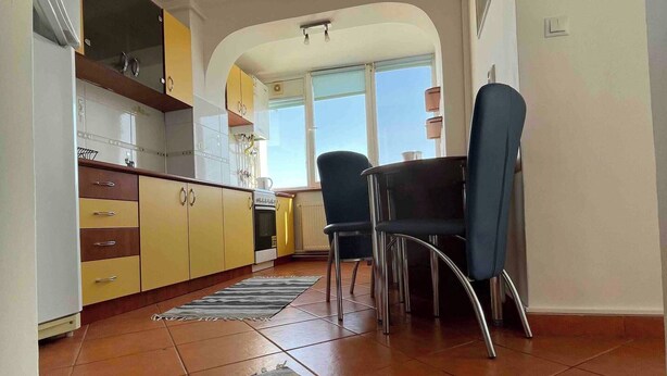 A kitchen with yellow cabinets, a dining table with chairs, and a large window. - Stunning Panoramic View Last Floor Save (Brasov)