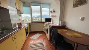 A compact kitchen with a washing machine, a dining area with a table and chairs, and a view of mountains through the window. - Stunning Panoramic View Last Floor Save (Brasov)