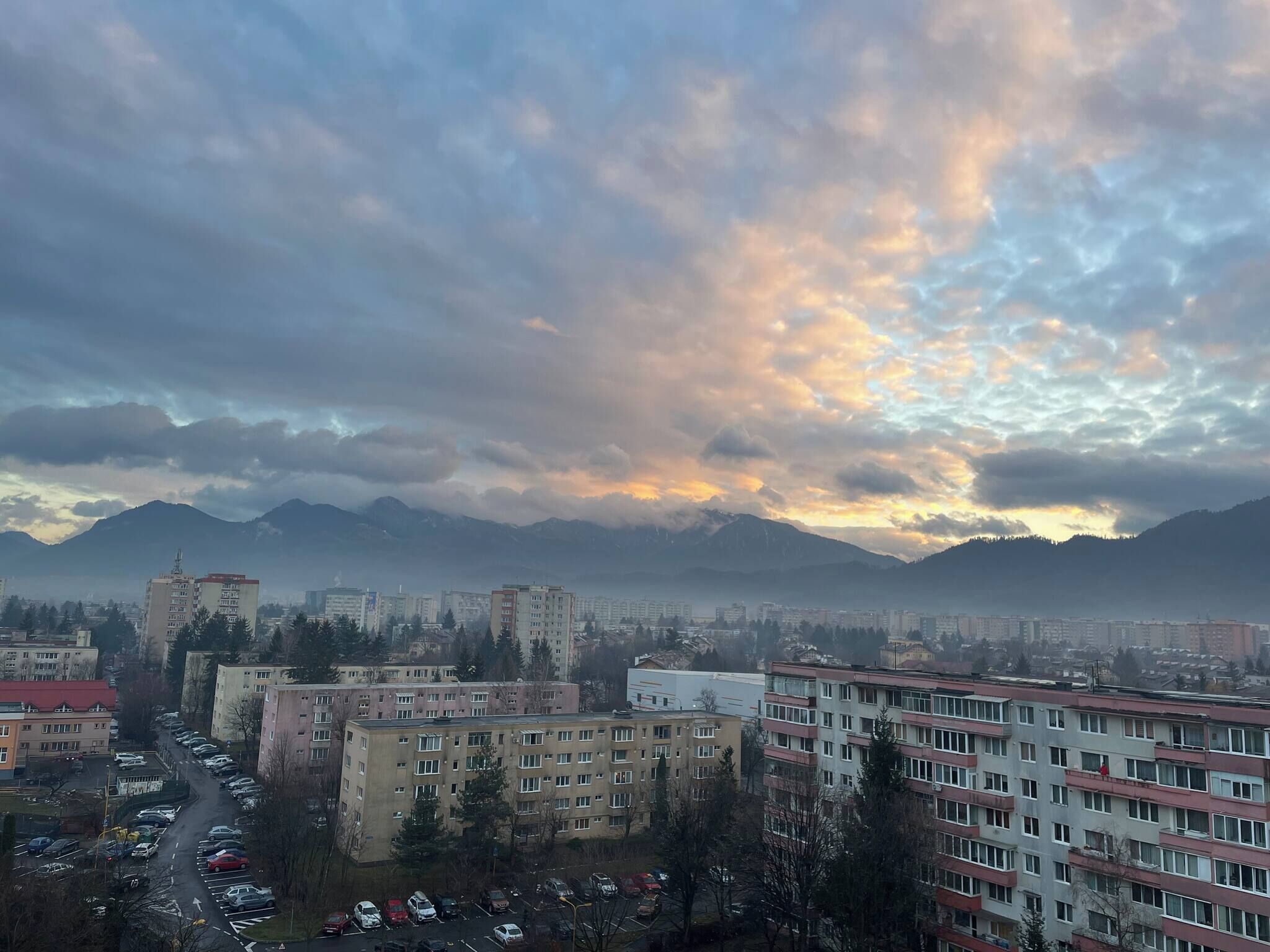 A cityscape with buildings, a parking lot, and mountains in the background.