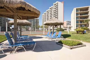 A resort area with lounge chairs, thatched umbrellas, and modern buildings in the background. - Beachfront Saida condo with Gulf views, resort pools, room for 6 and a $75 beach gear rental credit. (South Padre Island)