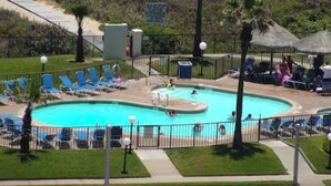 A swimming pool with blue water, surrounded by a fence, and equipped with lounge chairs and umbrellas. - Beachfront Saida condo with Gulf views, resort pools, room for 6 and a $75 beach gear rental credit. (South Padre Island)