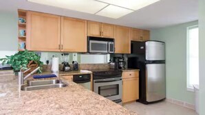A modern kitchen with granite countertops, wooden cabinets, a stainless steel refrigerator, a microwave, and a stove. - Beachfront Saida condo with Gulf views, resort pools, room for 6 and a $75 beach gear rental credit. (South Padre Island)