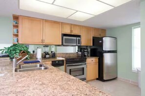 A modern kitchen with granite countertops, wooden cabinets, a stainless steel refrigerator, a microwave, and a stove. - Beachfront Saida condo with Gulf views, resort pools, room for 6 and a $75 beach gear rental credit. (South Padre Island)