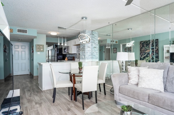 Una cocina moderna con armarios blancos, una isla central y una zona de comedor con mesa y sillas de vidrio.
