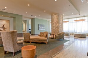 A spacious lobby with patterned furniture, a stone accent wall, and large windows. - 3BR Beachfront Condo at Sapphire with Stunning Ocean Views (South Padre Island)