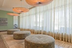 A room with three round ottomans, a patterned wall, and a large window with sheer curtains. - 3BR Beachfront Condo at Sapphire with Stunning Ocean Views (South Padre Island)