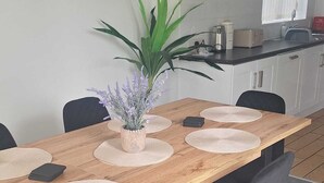 A dining area with a wooden table, black chairs, and a potted plant. - Modern large four bedroomed detached home (Toton)