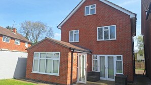 A two-story brick house with a small attached garage, a front door with a glass panel, and a visible garden area. - Modern large four bedroomed detached home (Toton)