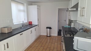 A kitchen with white cabinets, a black countertop, a stainless steel trash can, a toaster, and a stove. - Modern large four bedroomed detached home (Toton)