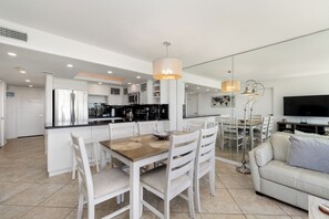 A modern kitchen with white cabinets, a dining area with a wooden table and chairs, and a living area with a sofa and TV. - First-floor beachfront Sea Vista condo with Gulf views, pools + $75 beach gear rental credit (South Padre Island)
