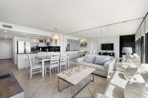 A modern kitchen with white cabinetry, a dining area with white chairs, a sofa with cushions, and a wooden coffee table. - 3BR Beachfront Condo at Sea Vista with Ocean Views (South Padre Island)