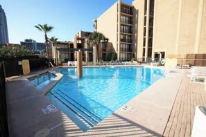 A swimming pool with a tiled deck, surrounded by high-rise buildings and palm trees. - First-floor beachfront Sea Vista condo with Gulf views, pools + $75 beach gear rental credit (South Padre Island)