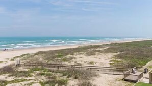 Blick auf einen Strand mit einer Holzpromenade, die zu einem Gebäude führt.