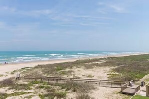 A beach view with a wooden walkway leading to a building. - First-floor beachfront Sea Vista condo with Gulf views, pools + $75 beach gear rental credit (South Padre Island)