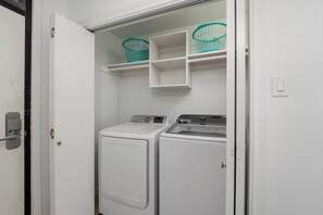 A laundry room with two white washing machines, a shelf with two baskets, and a door with a lock. - 3BR Beachfront Condo at Sea Vista with Ocean Views (South Padre Island)