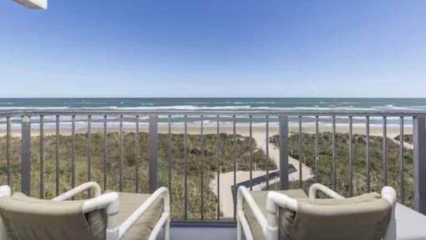 En balkon med to stole, der vender ud mod udsigten til stranden.